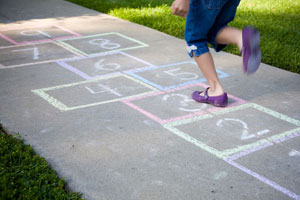 Girl hoping on one leg on pavement with chalk drawing.